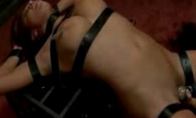 A busty girl is bonded to a Coop and is being stimulated with vibrating clips to her nipples
